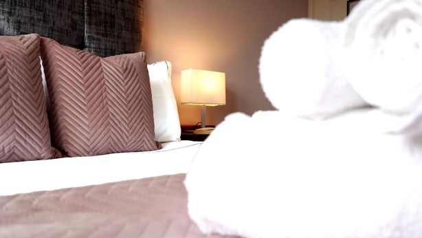Habitación de hotel con una cama, almohadas, una lámpara y una toalla enrollada.