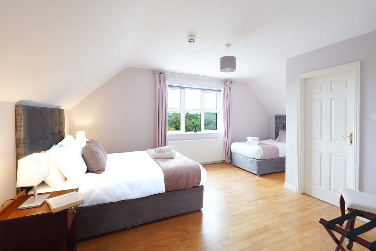 A bedroom with a large bed, a smaller bed, a desk with a lamp, and a chair.