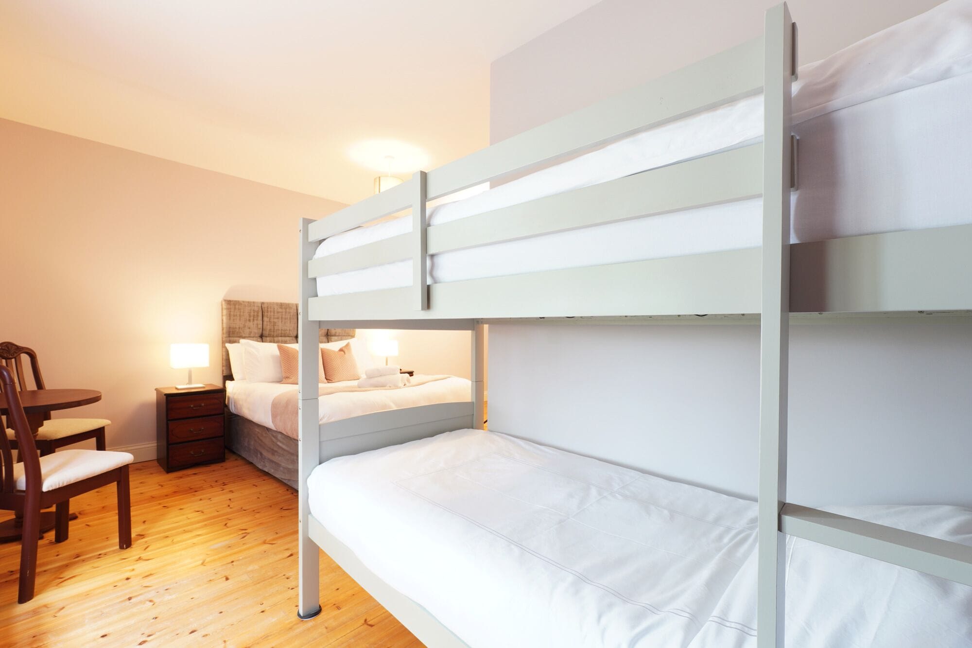 Quarto com beliche, uma cadeira de madeira e mesa de cabeceira com abajur.