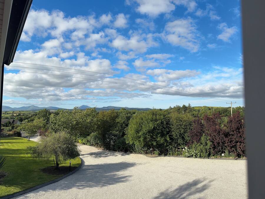Un camino de grava que conduce a una casa con vistas a un paisaje verde y montañas distantes.