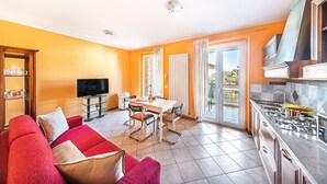 Ein Wohnzimmer mit einem roten Sofa, einem Esstisch mit Stühlen, einem Fernseher und einer Küche mit Herd.