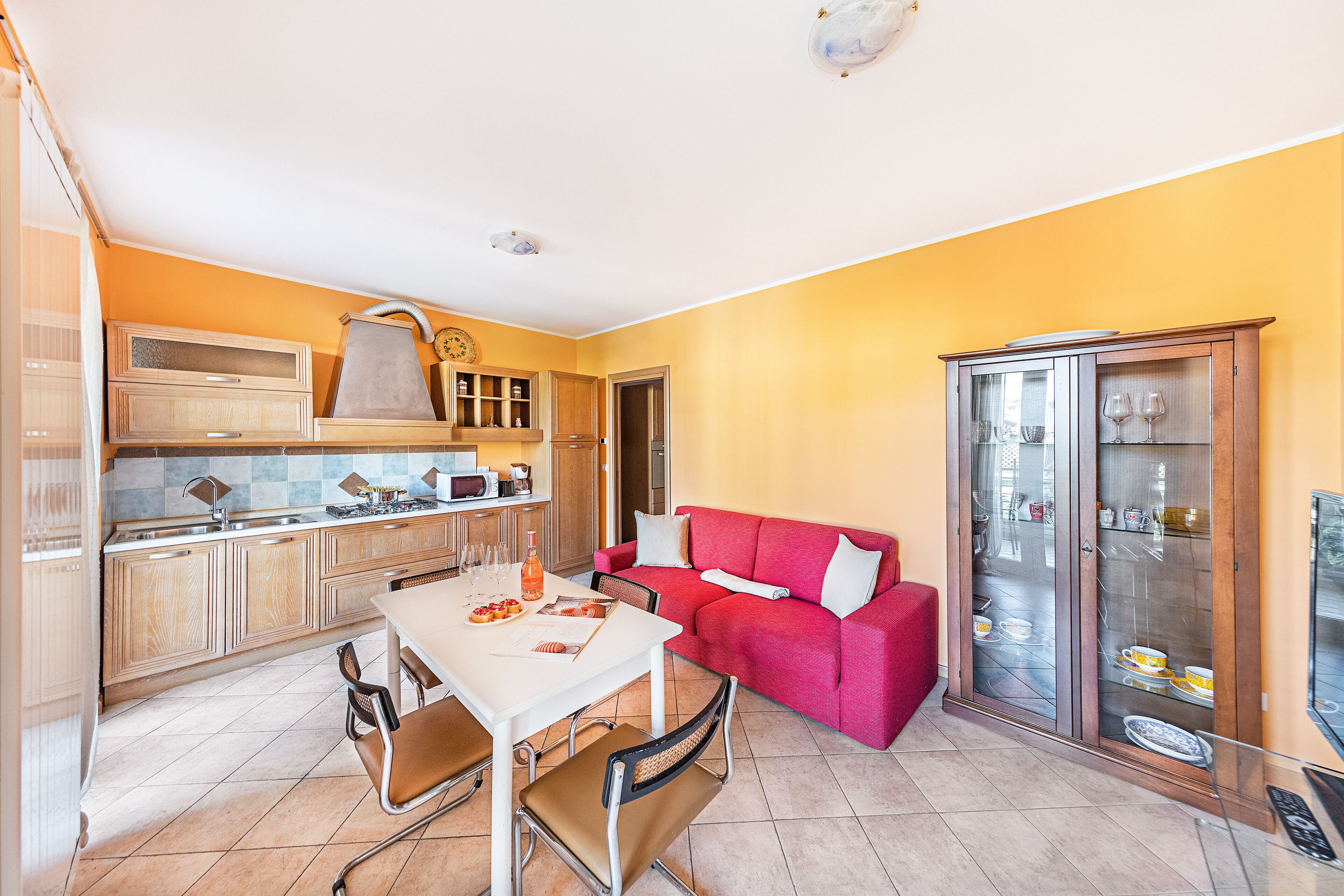 A compact living space with a dining area, a red sofa, and a glass-fronted cabinet with dishes.