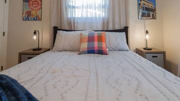 A neatly made bed with a patterned bedspread, two bedside lamps, and a window with sheer curtains.