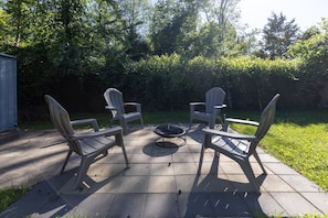 Un patio al aire libre con cuatro sillas Adirondack dispuestas alrededor de un pozo de fuego circular.