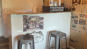 A reception area with a wooden counter, two metal stools, a 'WELCOME' sign, and a wall covered with newspaper clippings. - Nana’s Bunkhouse is a small little efficiency located in Houston, MO.  (Houston)