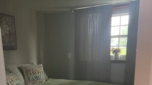 A bedroom with a bed, pillows, a window with curtains, and a wall with a framed picture. - Nana’s Bunkhouse is a small little efficiency located in Houston, MO.  (Houston)