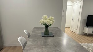 Een eetgedeelte met een grijze tafel, witte stoelen en een vaas witte bloemen.