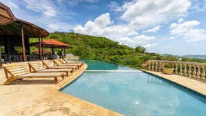 A swimming pool with wooden loungers and a covered seating area, surrounded by lush greenery and a clear sky. - Casa Rebanada de Vida (Mar Vista)