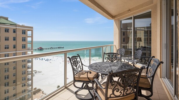 A balcony with a table and chairs overlooking a beach and pier. - Sweeping Gulf and Bay views on Clearwater Beach, 15th floor Penthouse 3 BR/3BA (Clearwater)
