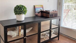 Ein Wohnzimmer mit einem schwarzen Konsolentisch, einer Topfpflanze, einem gerahmten Buch und einem an der Wand befestigten Flachbildfernseher.