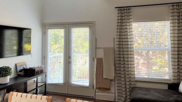 Ein Zimmer mit Deckenventilator, einer Schiebetür, einem rahmenlosen schwarzen Fenster, einer schwarzen Couch und einem kleinen Tisch mit einer Pflanze.