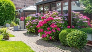 A garden with a brick pathway, a wooden pergola, and a variety of flowering shrubs. - Pension Nordlicht (Esens)