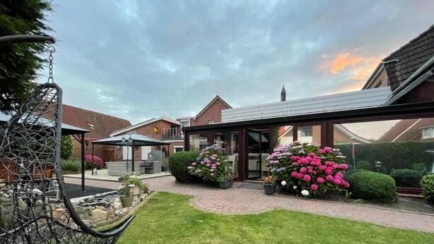 A residential garden with a swing chair, a pathway, and flower beds. - Pension Nordlicht (Esens)
