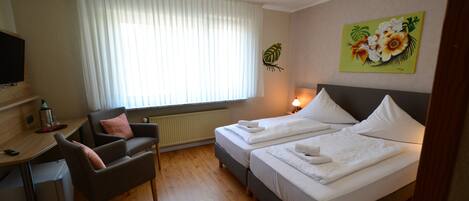 Hotelkamer met twee bedden, een bureau, een stoel, een televisie en een raam met gordijnen.