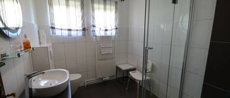 A modern bathroom with a large white sink, a toilet, a glass shower enclosure, and a small vanity table.