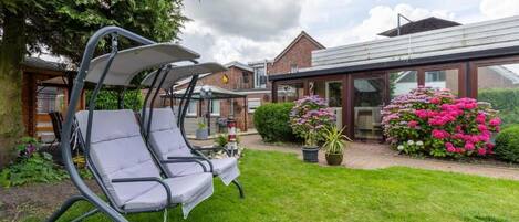 A patio with two lounge chairs, a brick building, and a glass conservatory.