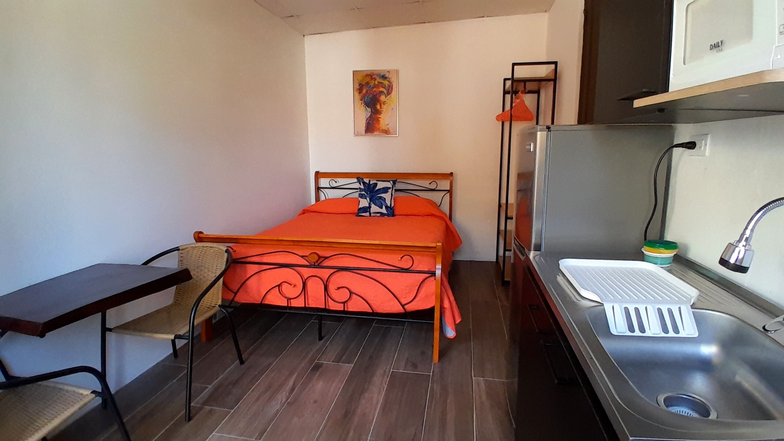 Una habitación pequeña con cama, un escritorio, una silla, un lavamanos y ducha.