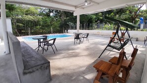 Un espacio al aire libre techado con piscina, mesas, sillas y un columpio.