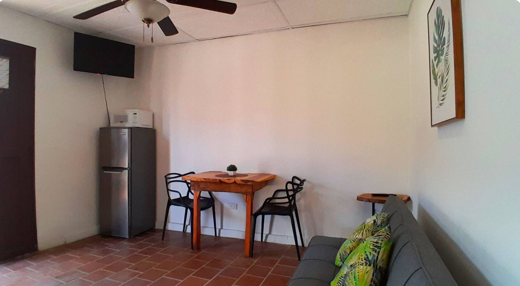 Un espacio habitable compacto con kitchenette, una zona de comedor con dos sillas, un sofá y un ventilador de techo.