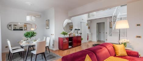 A modern living room with a red sofa, a dining area with a glass table, and a hallway leading to a staircase.
