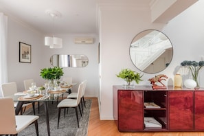 Uma sala de jantar moderna com mesa de vidro, cadeiras brancas e um armário vermelho com objetos decorativos.