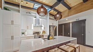 A modern kitchen with white cabinetry, a large island with bar stools, stainless steel appliances, and pendant lighting.