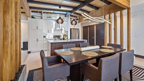 A modern kitchen with white cabinets, a central island, and a dining area with a dark table and grey chairs.