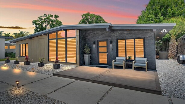 A modern house with large windows, a patio with seating, and a gravel driveway.