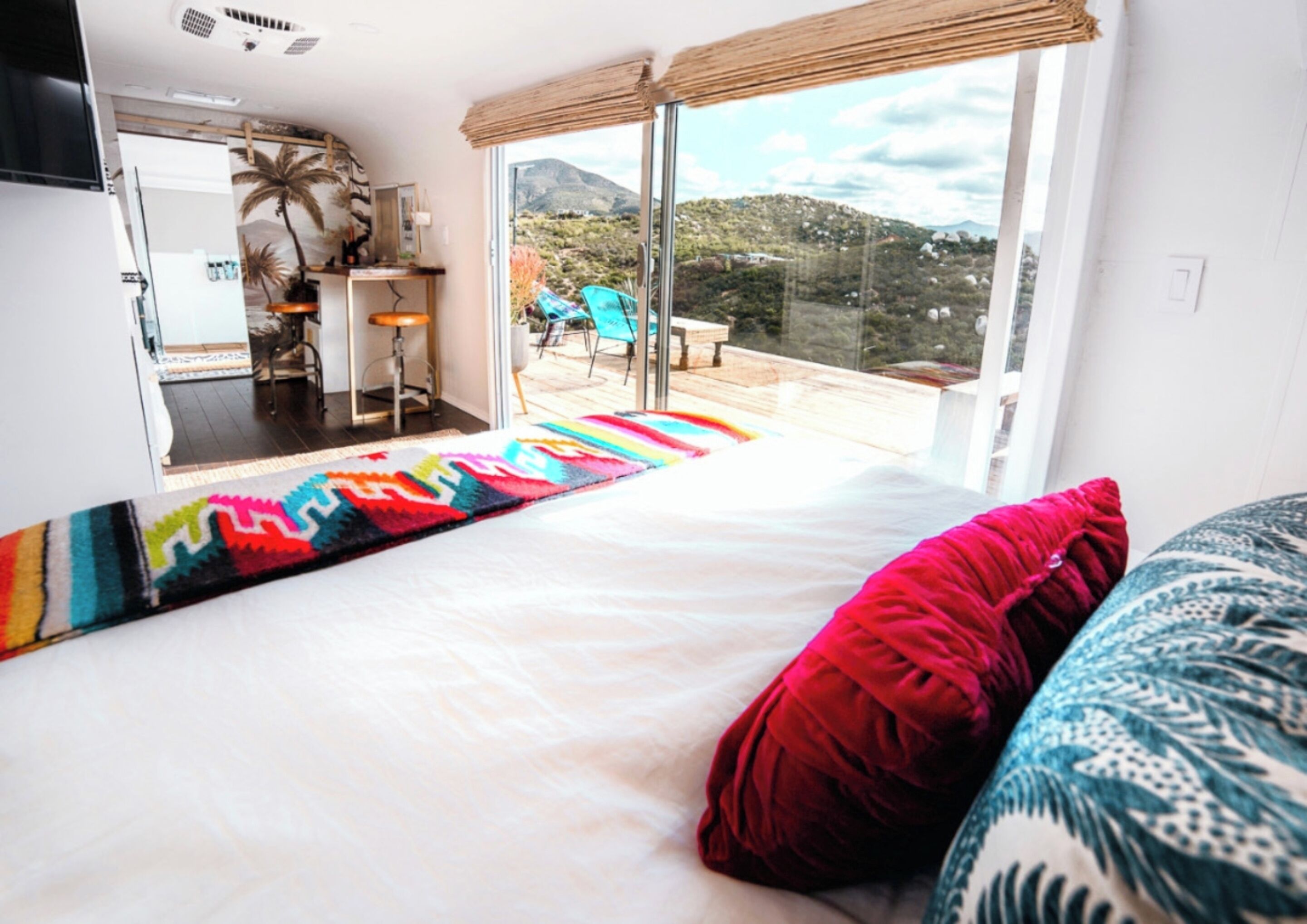 Een slaapkamer met een groot bed, een kleurrijk vloerkleed en uitzicht op een terras met stoelen en een tafel.