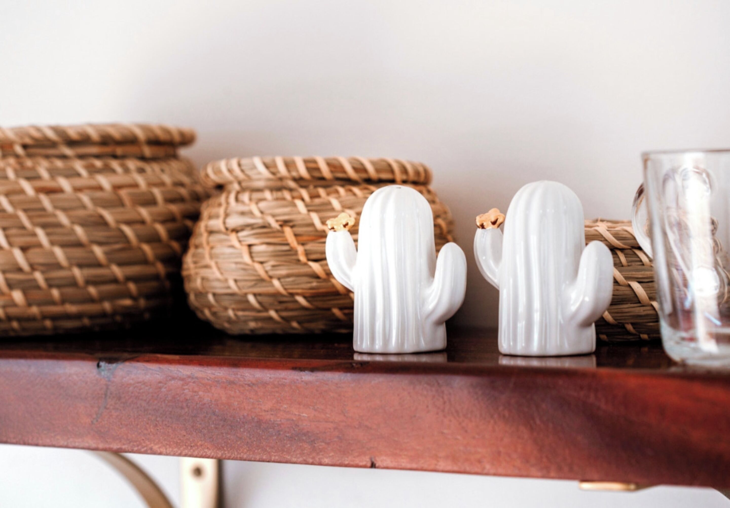 Une étagère en bois avec des paniers tressés et deux salières et poivrières blanches en forme de cactus.
