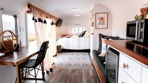 A compact RV interior with a bed, kitchenette, and a dining area. - Arre Lulu Baja (Valle de Guadalupe)
