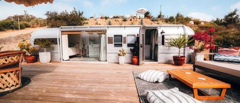 Una casa móvil con la puerta abierta, una terraza de madera y mobiliario exterior.