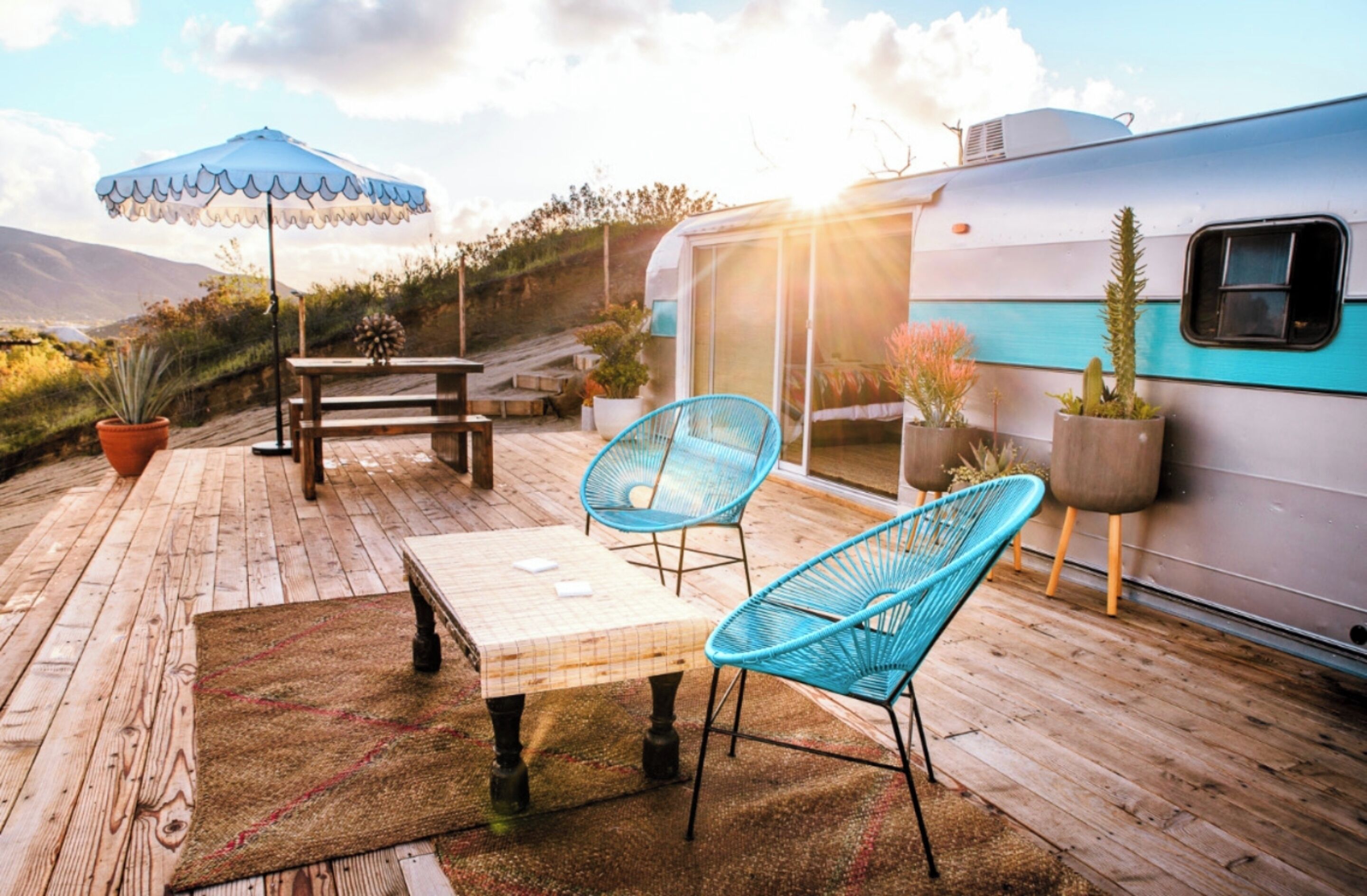 A wooden deck with a table and chairs, potted plants, and a blue umbrella.