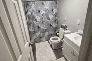 A bathroom with a toilet, a sink, and a shower curtain with a leaf pattern. - Coastal Cottage- Apalachicola- Golf Cart Rental (Apalachicola)