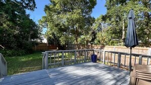 Una terrassa de fusta amb barana metàl·lica, un cubell blau i una ombrel·la.