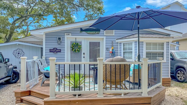A coastal cabin with a wooden deck, a covered seating area, and a large umbrella. - Myrtle Beach 'Coastal Cabana' w/ Resort Amenities! (Myrtle Beach)