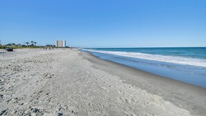 A beach with a clear sky, sandy shore, and a few buildings in the distance. - Myrtle Beach 'Coastal Cabana' w/ Resort Amenities! (Myrtle Beach)