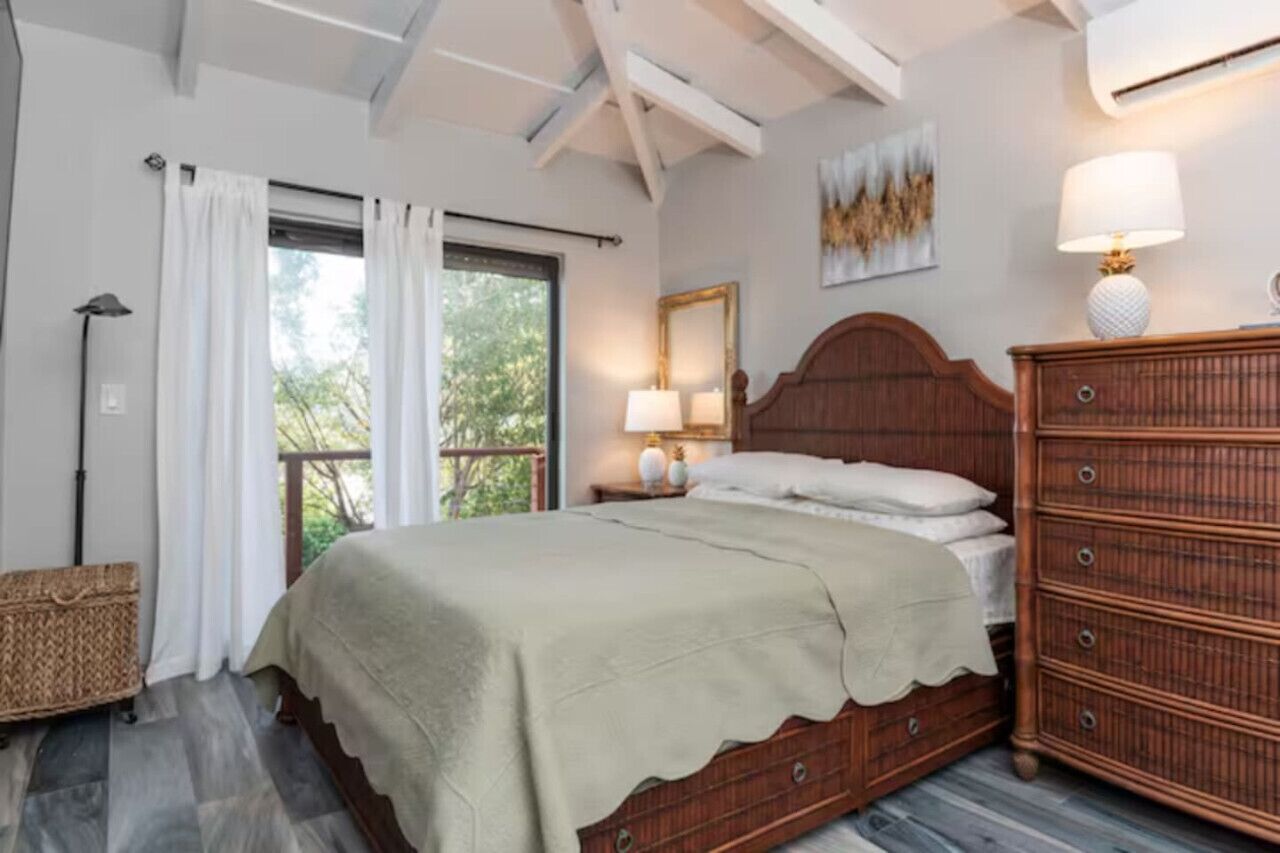 A bedroom with a wooden bed, a nightstand with lamps, a dresser, and a window with curtains.