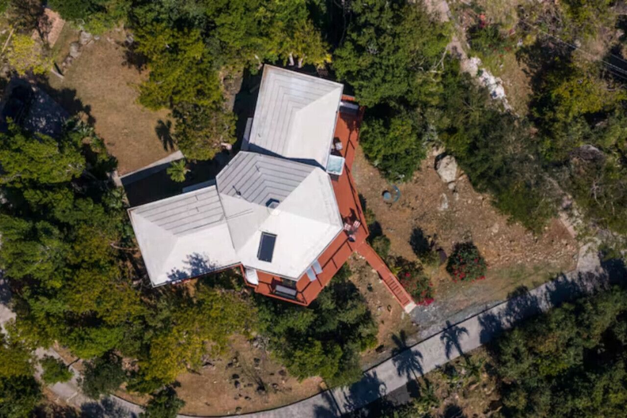An aerial view of a house with a sloped roof, surrounded by dense greenery.