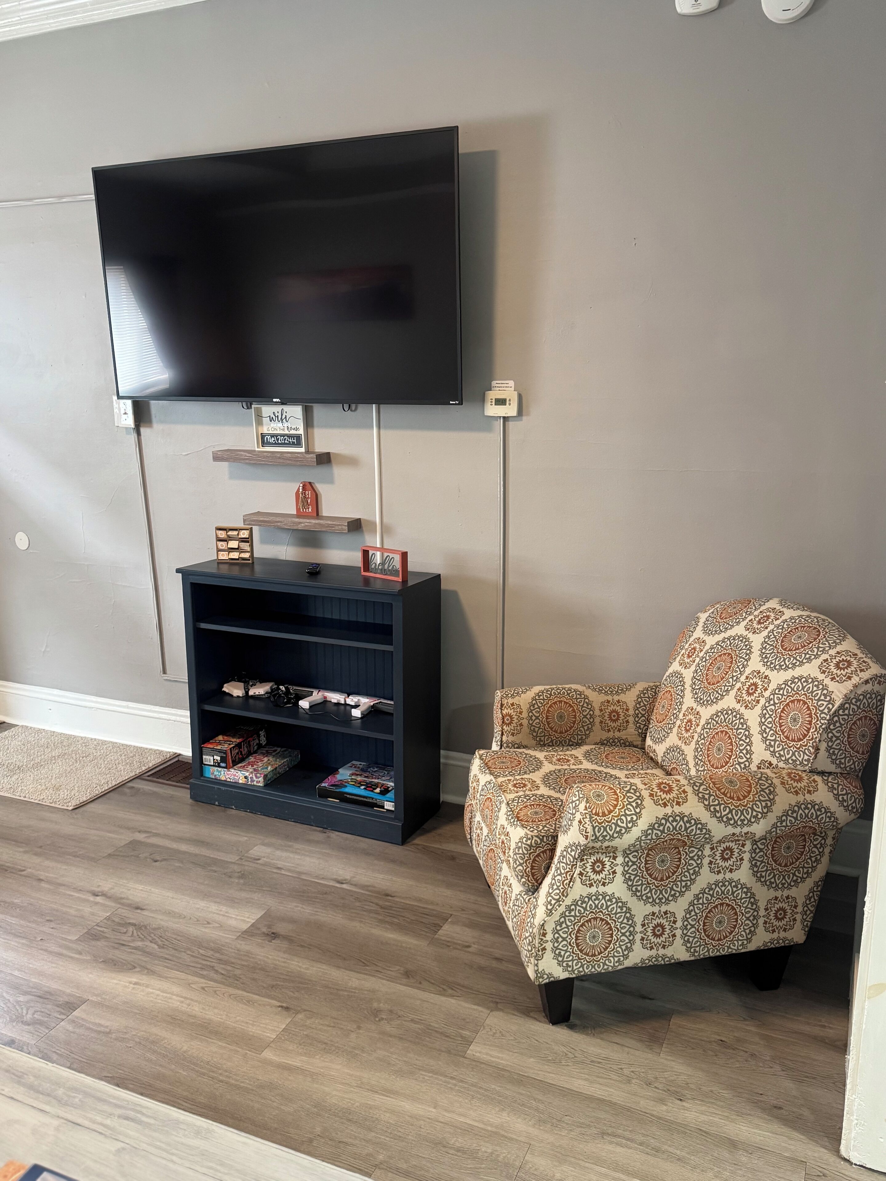 A living room with a flat-screen TV mounted on the wall, a wooden entertainment unit below, and a patterned armchair.