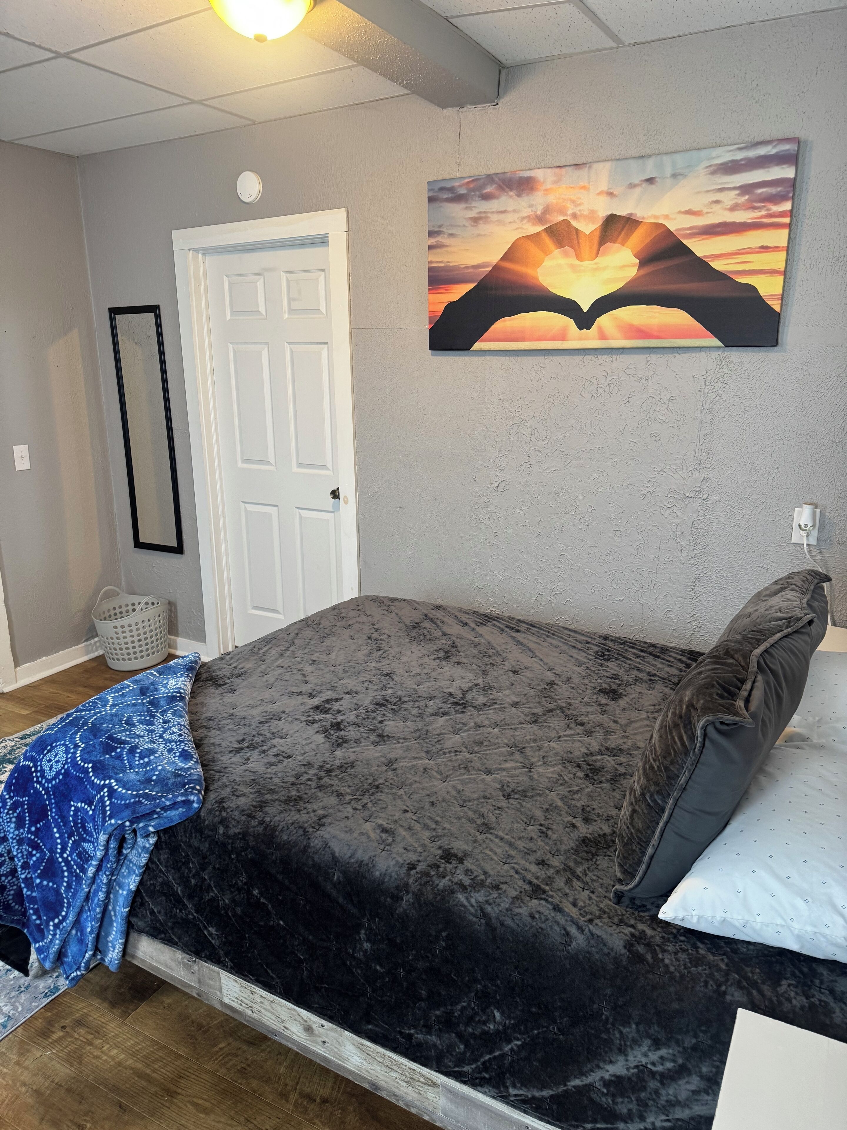 Une chambre à coucher avec un lit, une porte, un tableau accroché au mur et un luminaire au plafond.