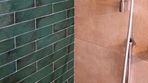 A shower with a chrome finish and a wall with green tiles.