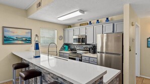 Una cocina moderna con una isla grande, taburetes de bar, electrodomésticos de acero inoxidable y un cuadro en la pared.