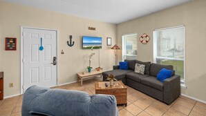 Una sala de estar con un sofá gris, un sillón azul, una mesa de centro y un televisor en la pared.