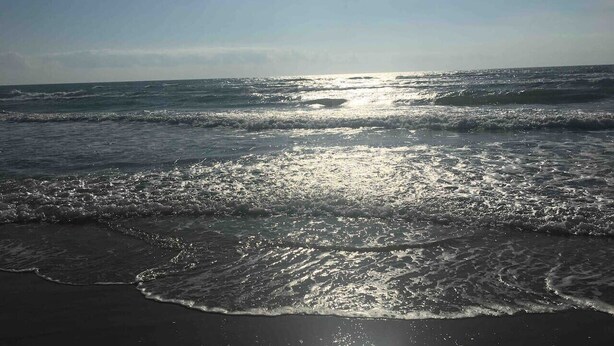 Una playa con olas y el sol reflejándose en el agua.