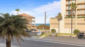 Un hotel frente al mar con vista al océano, aparcamiento y palmeras.