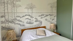 Un dormitorio con cama, un mural en la pared con escena de playa, una lámpara de noche y una mesita de noche.