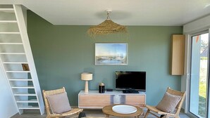 Una sala de estar moderna con un sofá, sillas, una mesa de comedor, un televisor de pantalla plana y una escalera.