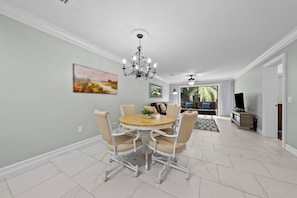 A dining area with a round table, chairs, a chandelier, and artwork on the walls.