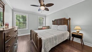 Un dormitorio con una cama de madera, un ventilador de techo, un aparador y una mesita de noche con una lámpara.